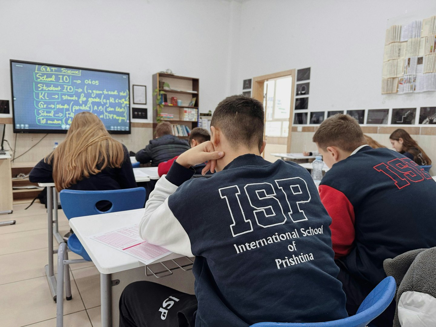 Studenti siedono alle scrivanie lavorando a compiti in classe.