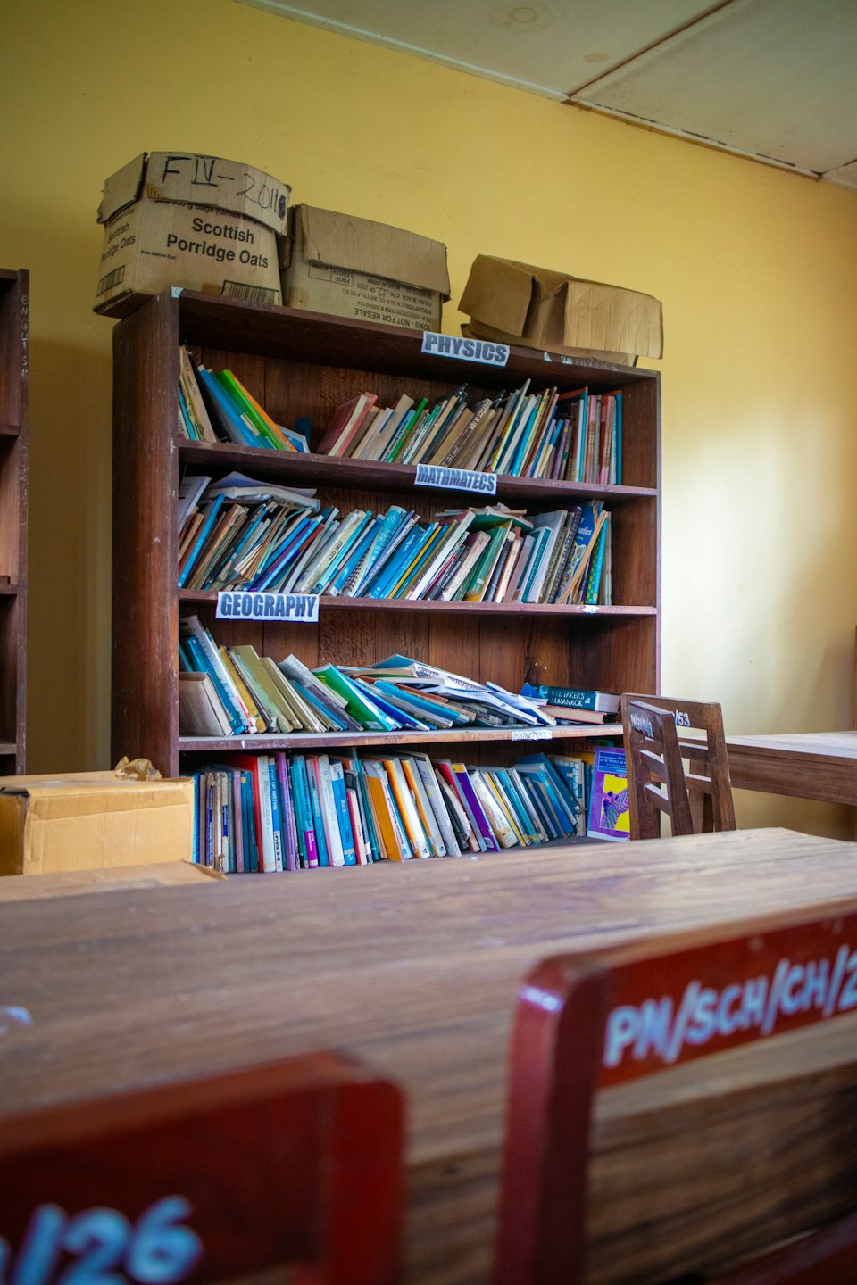 Una libreria di legno disordinata, piena di libri e scatole in un'aula.
