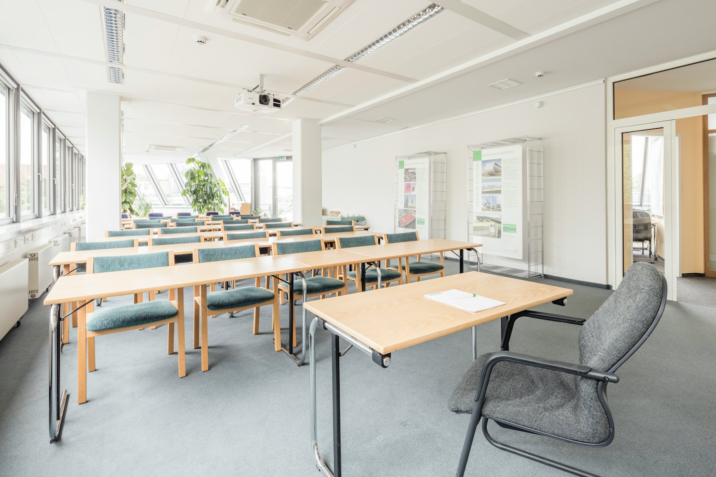 Aula moderna con tavoli in legno chiaro e sedie color ottanio.